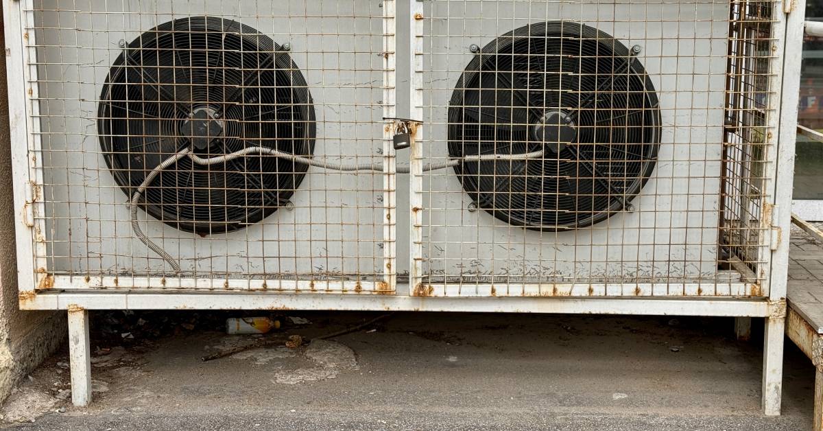 A pair of large industrial fans used for evaporative cooling sitting in a protective metal cage outside of a building.