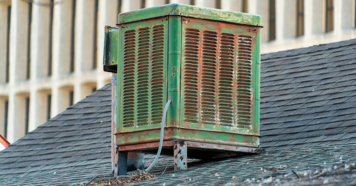 A swamp cooler mounted to the roof of a building. The metal is showing signs of corrosion and the green paint is fading.