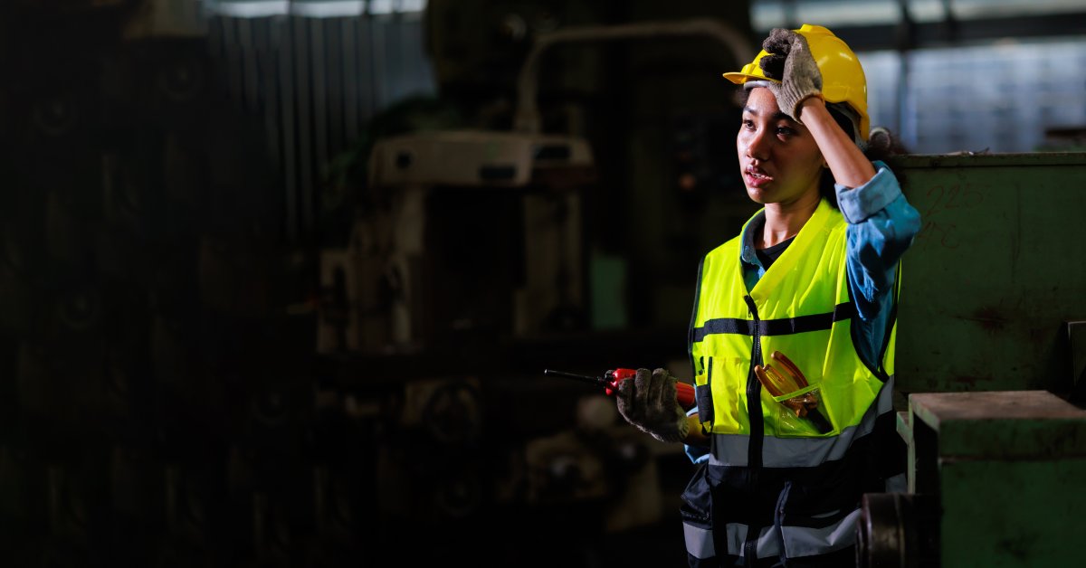 A woman wearing a yellow hard hat and a high-visibility vest sweating after overexerting herself at work.