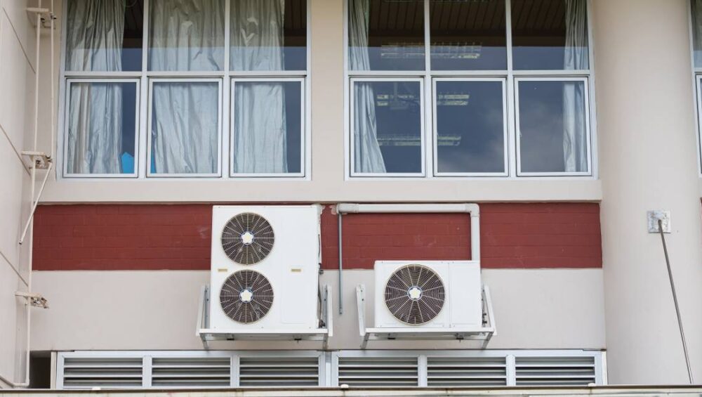 A building with a red stripe running across the outside wall. There’s an evaporative cooler installed on the side of it.