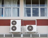 A building with a red stripe running across the outside wall. There’s an evaporative cooler installed on the side of it.