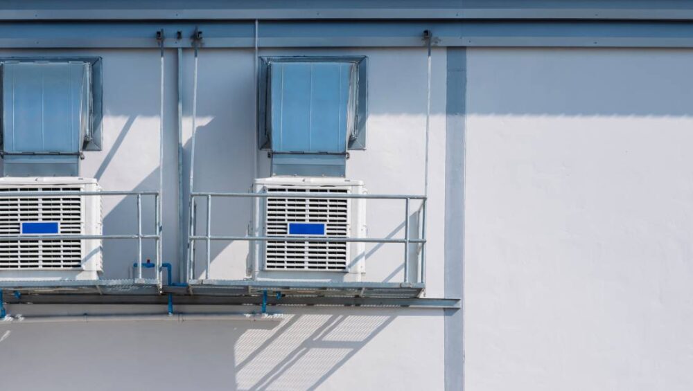 Two white evaporative coolers sitting on balconies next to one another on the side of a building during the day.