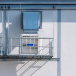 Two white evaporative coolers sitting on balconies next to one another on the side of a building during the day.