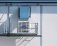 Two white evaporative coolers sitting on balconies next to one another on the side of a building during the day.