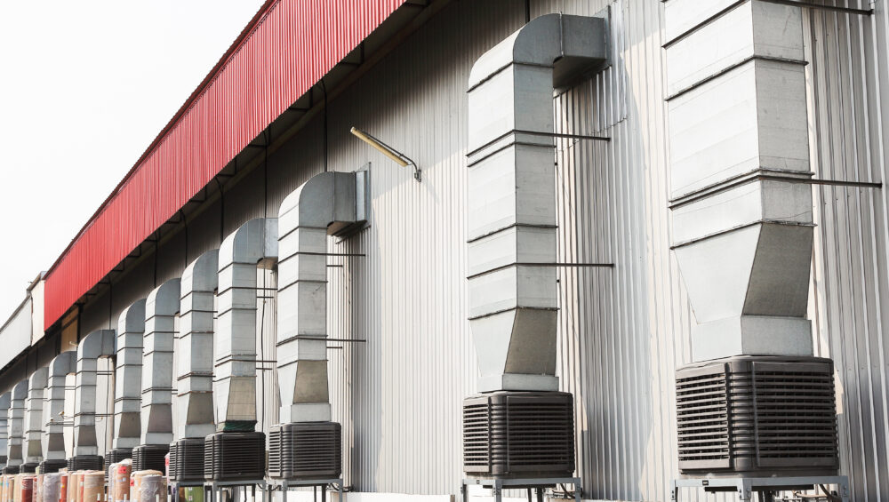 A long row of evaporative cooling units on top of metal stands connected to airducts outside of a building.