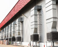 A long row of evaporative cooling units on top of metal stands connected to airducts outside of a building.