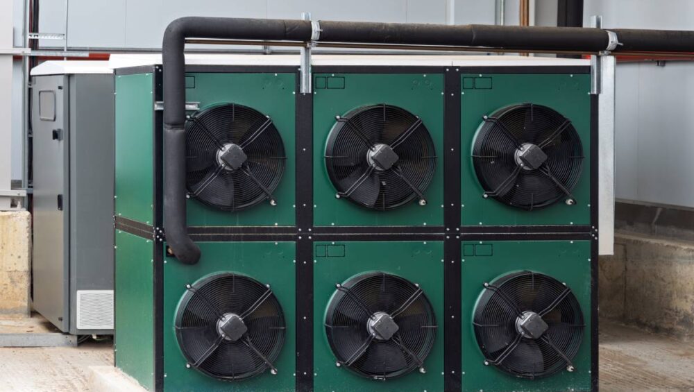 An industrial evaporative cooling system with multiple fans and green casing next to another metallic unit near a building.