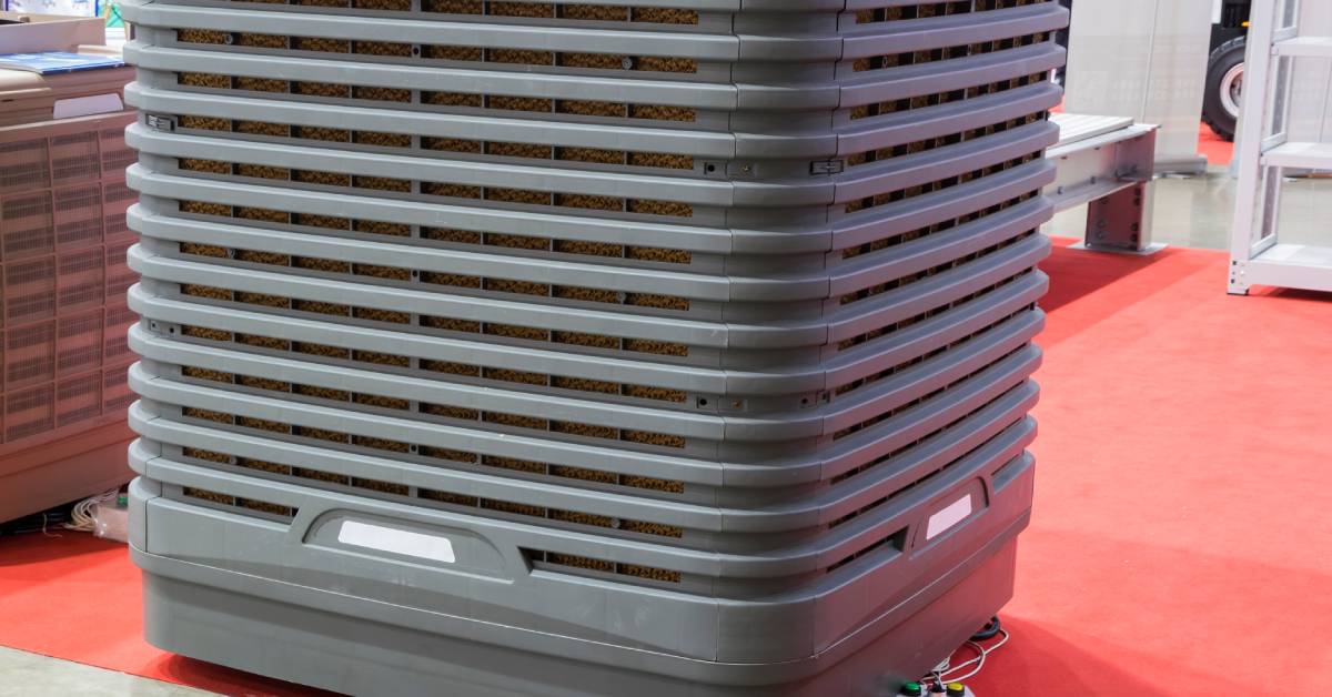 A close-up of a modern evaporative cooling unit displayed on a red rug and surrounded by other equipment.